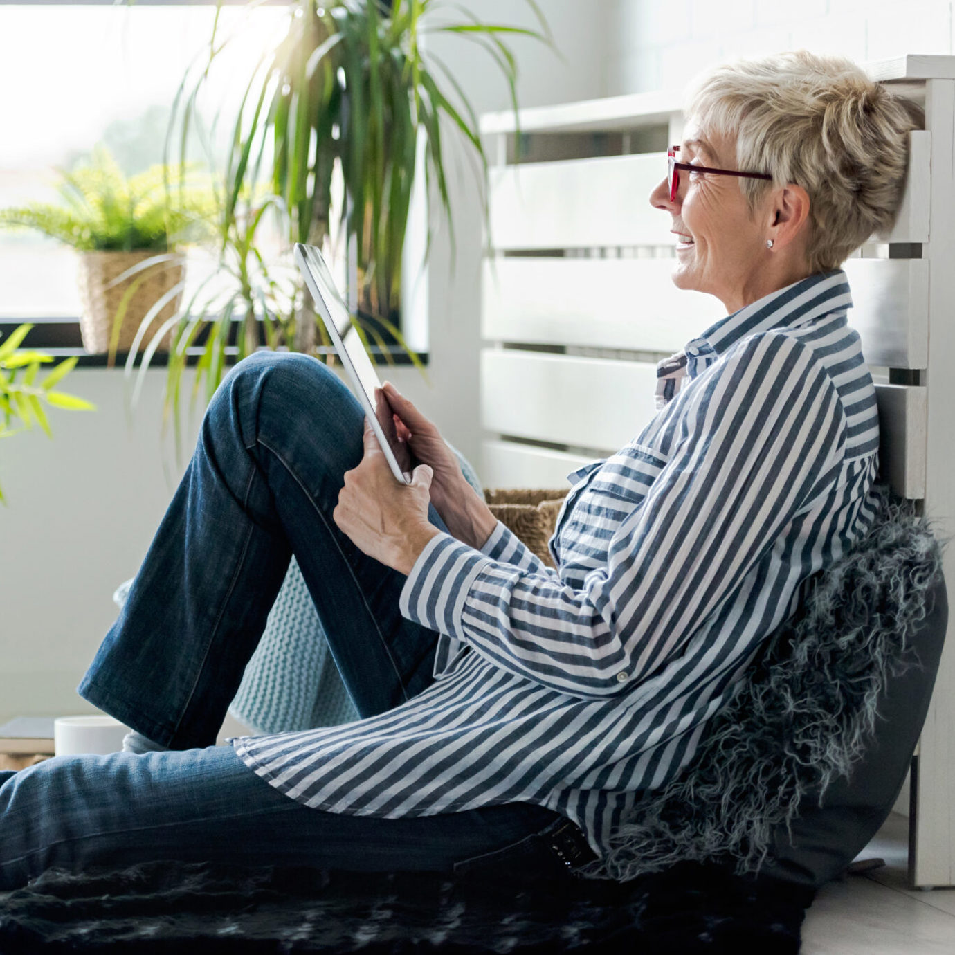 Senior woman wearing glasses relaxing on a sofa and reading a tablet at home.