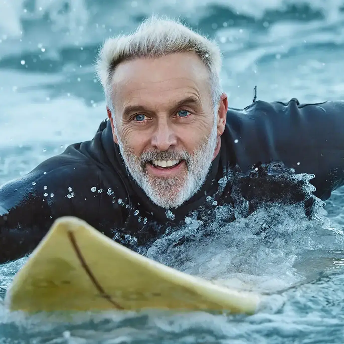 Smiling senior man with grey hair surfing on a bodyboard in the sea.