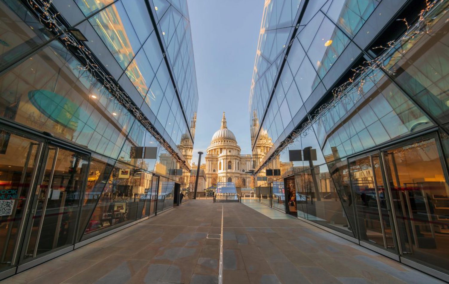 A modern city road with glass buildings either side facing a traditional city building at the end of a road