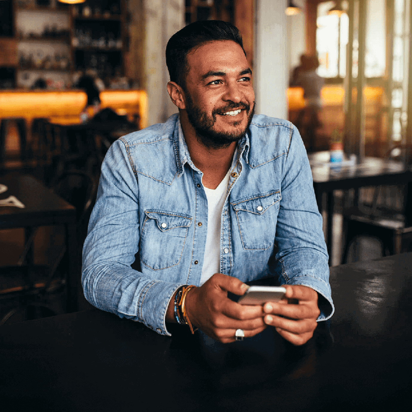 Smiling man sitting in a café and holding a smartphone.