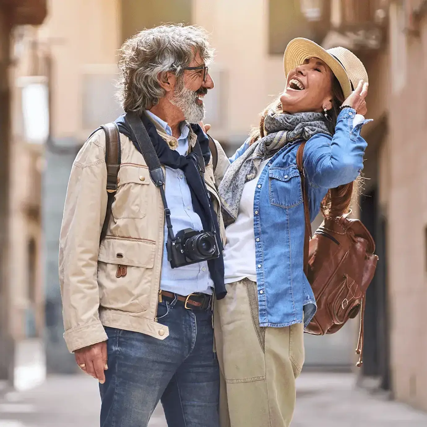 Smiling senior couple with backpacks enjoying a walk together along a cobbled street.