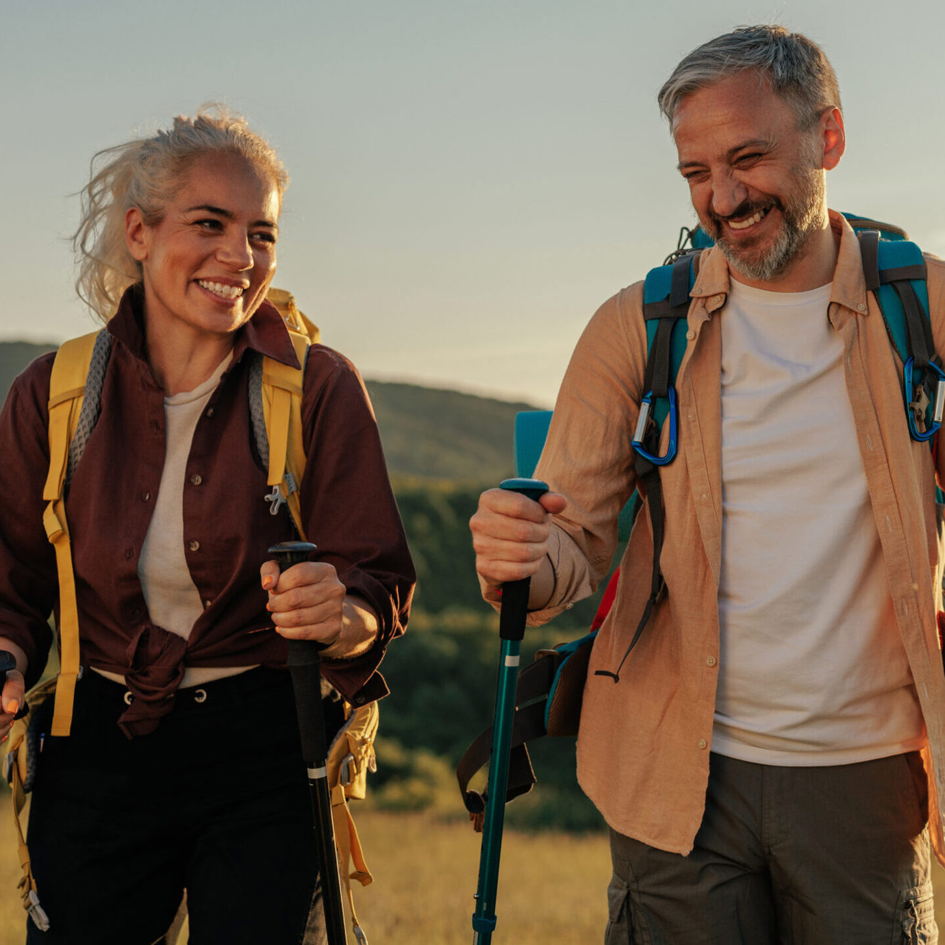 Smiling couple hiking outdoors with backpacks and walking poles.