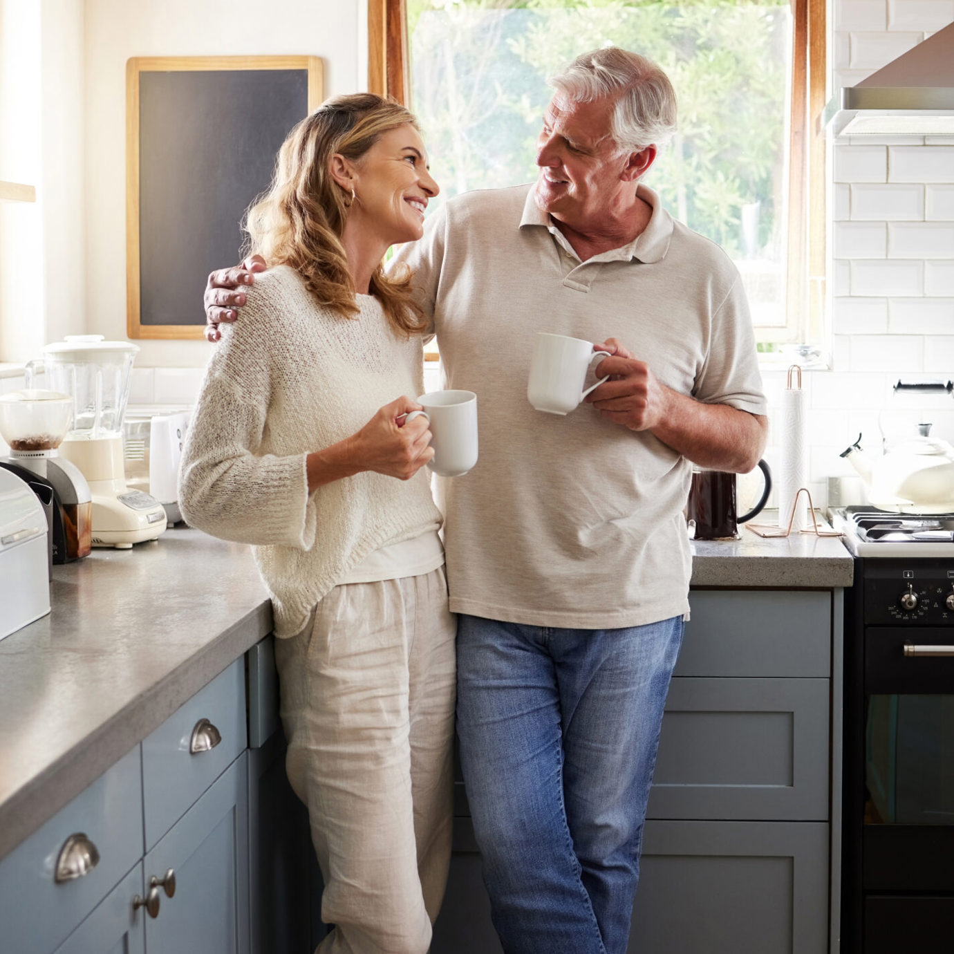 Happy senior couple smiling and enjoying a cup of coffee together in their kitchen.