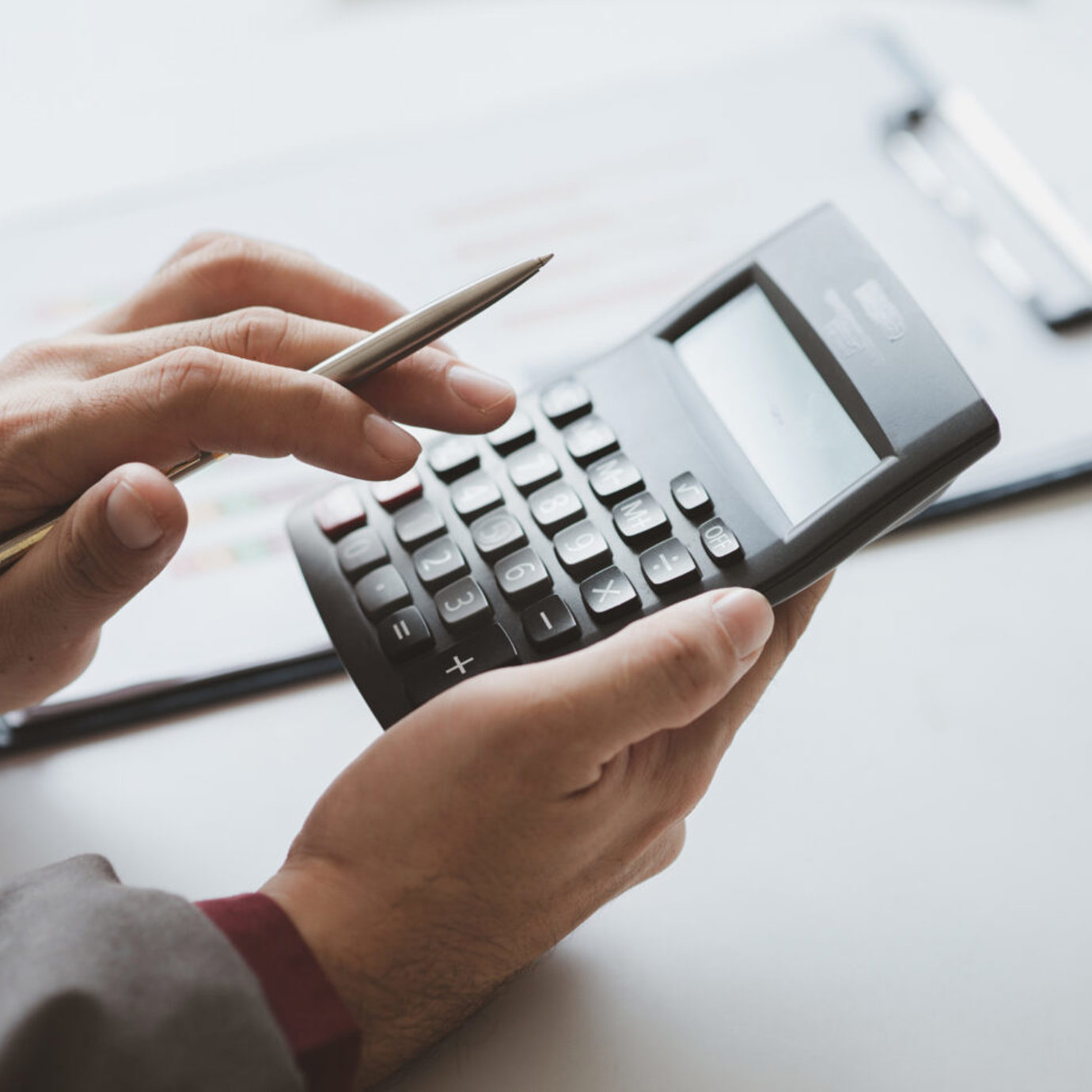 Close-up of a person using a calculator and smartphone while reviewing finances at a desk.