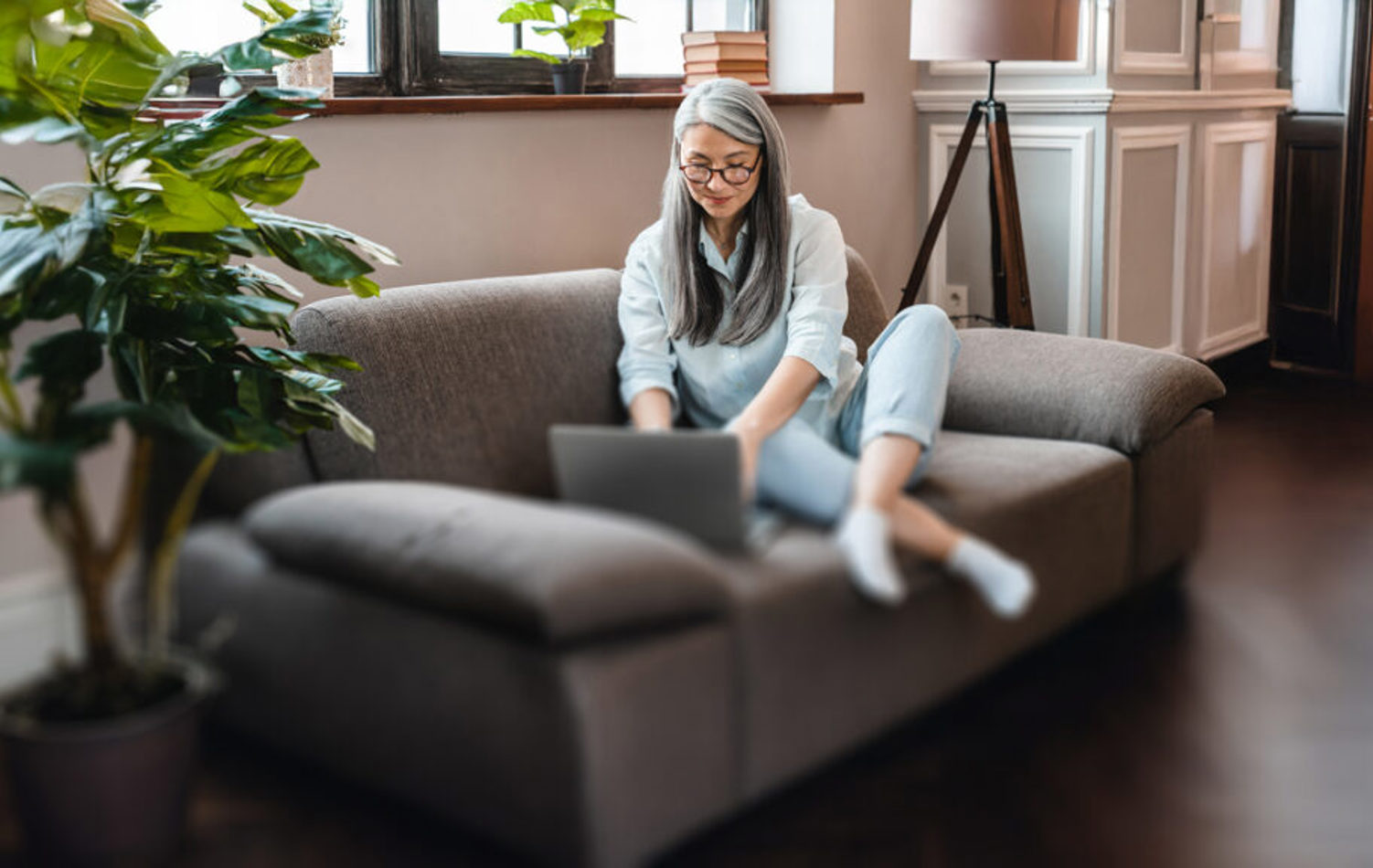 A woman sat on the sofa beside a plant working on her laptop