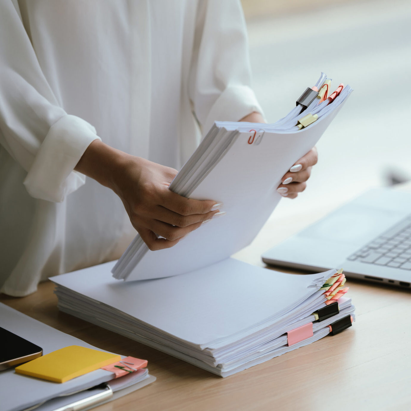 Person reviewing paperwork at a desk with a laptop, stationery and a takeaway coffee.