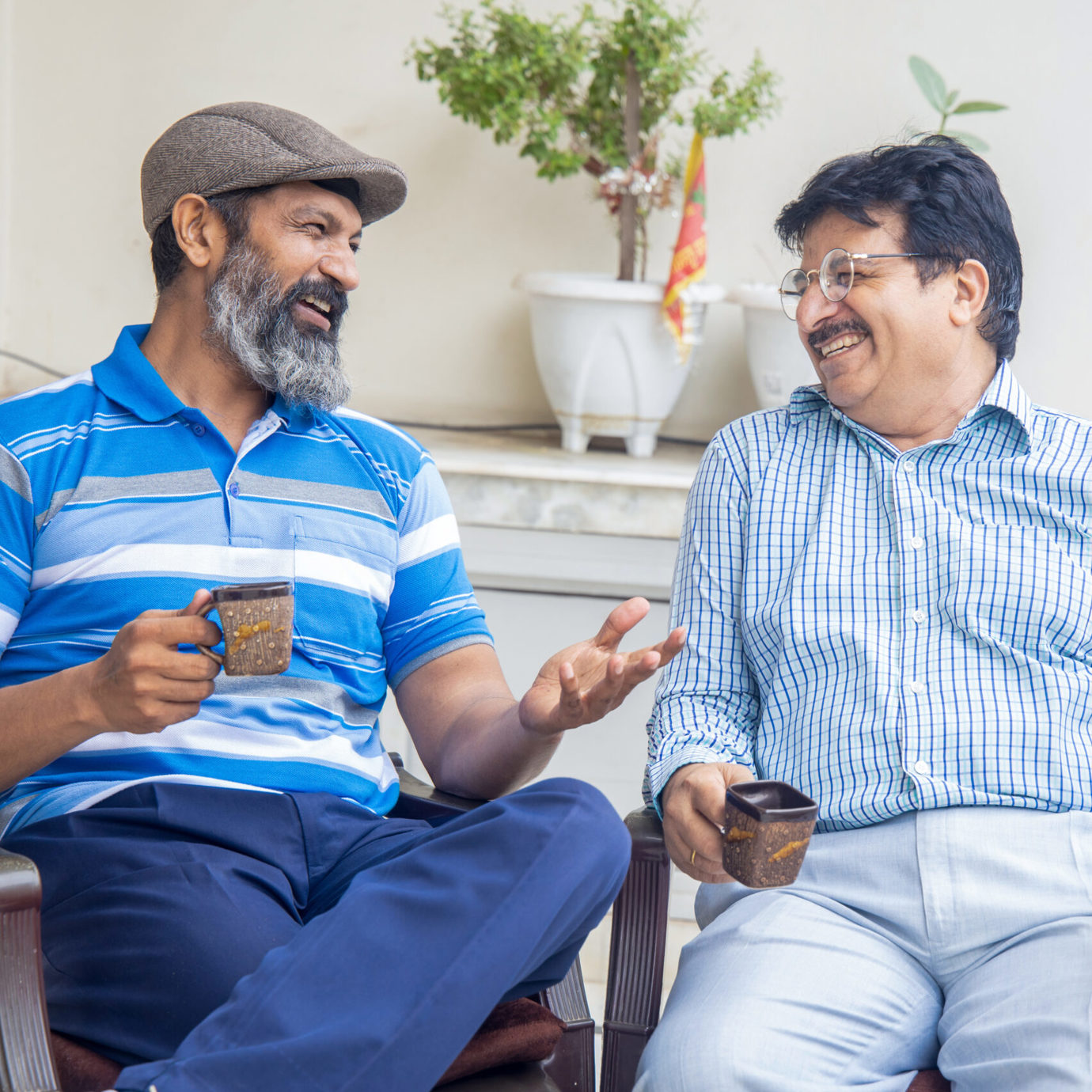 Two smiling men sitting together, chatting and enjoying cups of coffee.