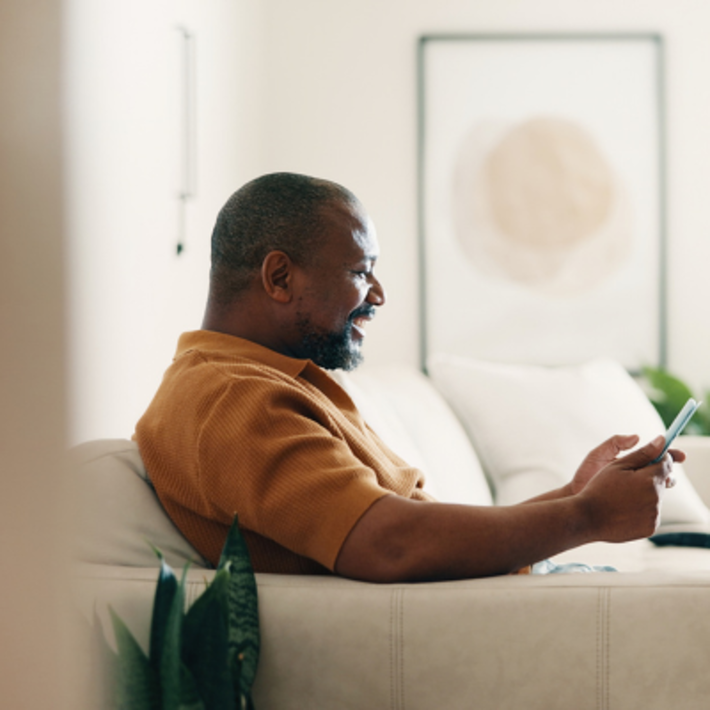 Middle-aged man relaxing on a sofa at home while looking at his mobile phone.