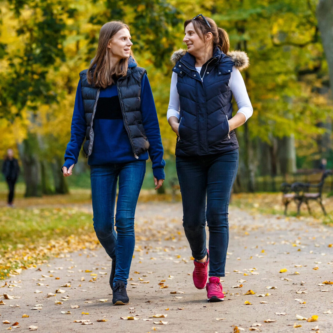 Two women enjoying a relaxing walk together through a peaceful park on an autumn day.