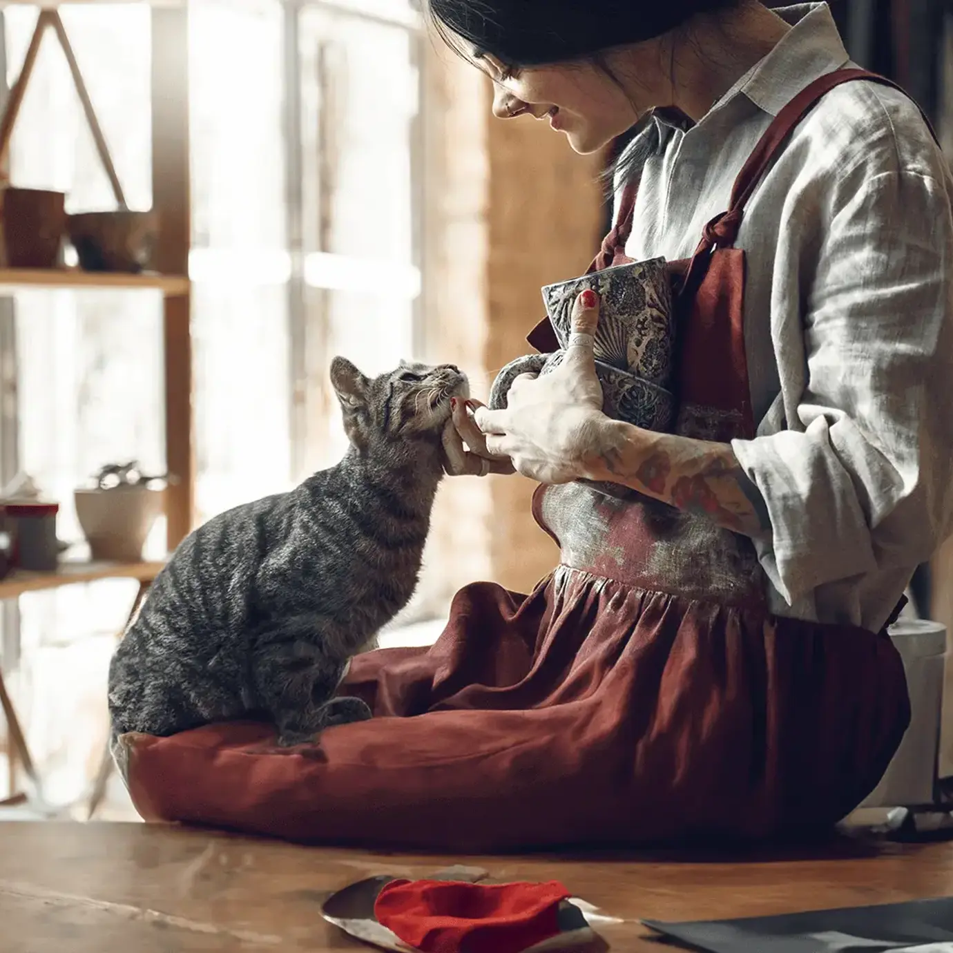 Young lady sitting by a window and petting a tabby cat in a cosy living room. 