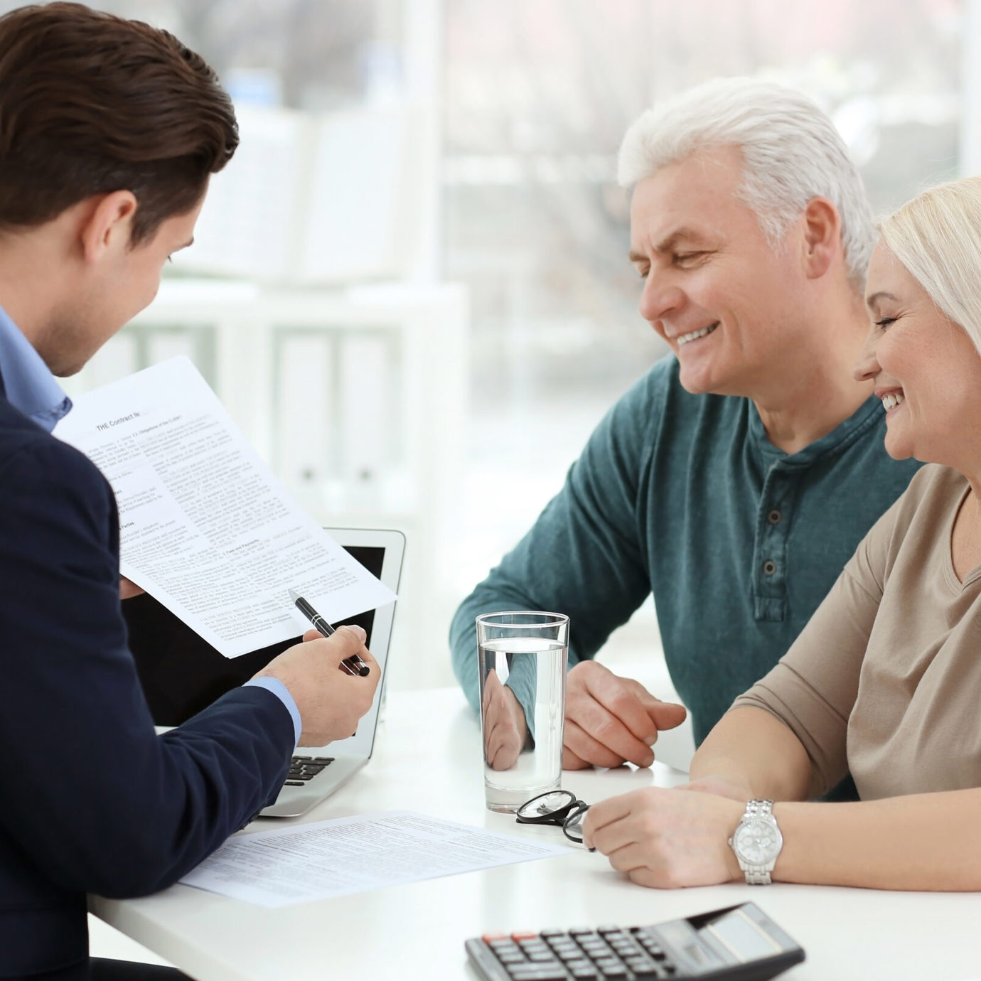 Smiling senior couple discussing paperwork with a financial adviser during a consultation.