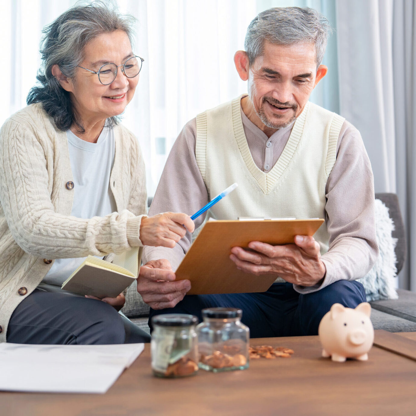 Senior couple sitting together on a sofa, reviewing documents and using a tablet at home.