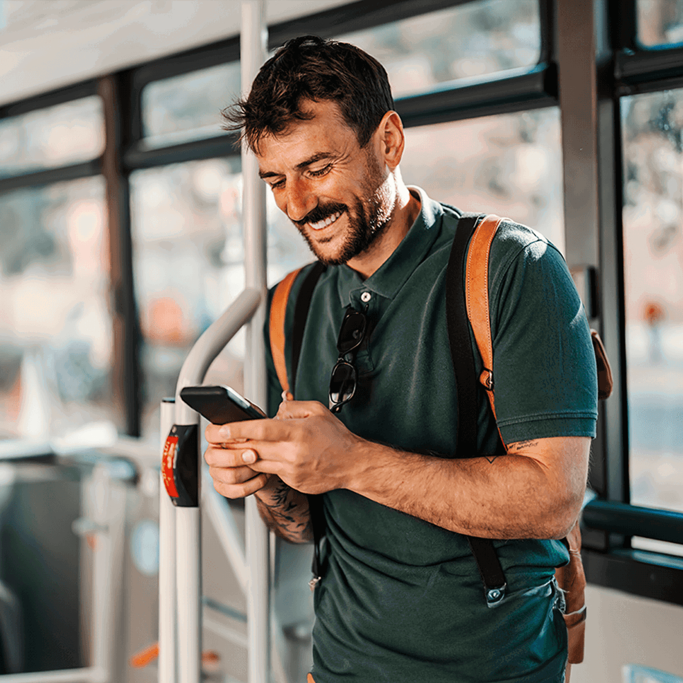 Smiling man wearing a backpack and checking his smartphone while travelling on public transport.